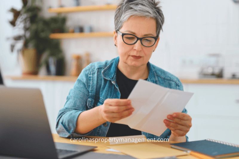 A focused homeowner sitting at a kitchen table reviewing documents with a laptop and notebook nearby. This image illustrates how Carolina Property Management LLC assists homeowners in effectively managing property-related finances and decisions.