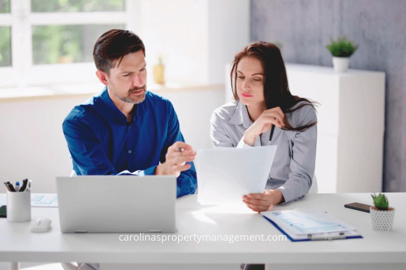 A man and woman sitting at a desk in a bright office, reviewing documents and discussing property management strategies. This image highlights the personalized service and expertise provided by Carolina Property Management LLC to support property owners in making informed decisions.