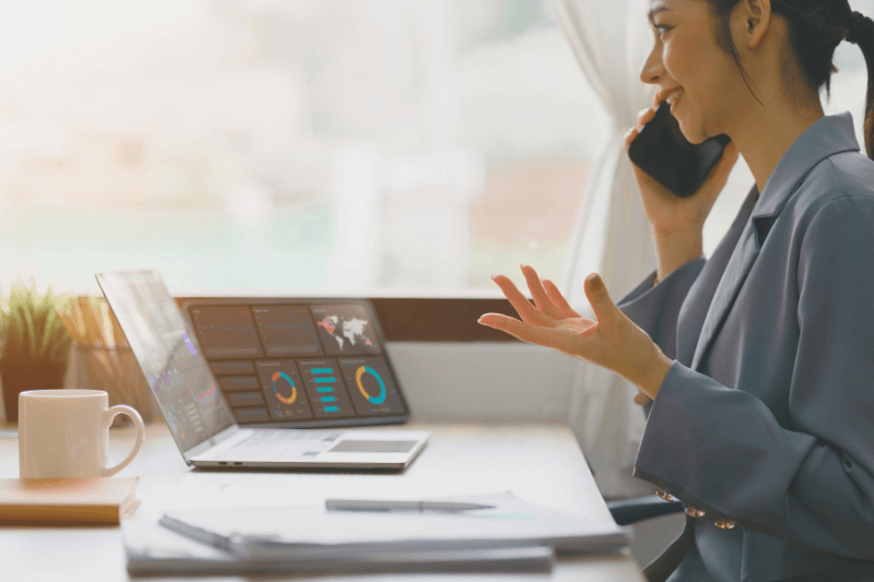 A property manager in a professional office environment having a phone discussion while analyzing property performance data on a laptop screen. The workspace includes a cup of coffee, documents, and vibrant charts displayed on the laptop. This image conveys the proactive communication and data-driven approach Carolina Property Management LLC takes when managing properties for landlords, ensuring informed decisions and optimal property performance.