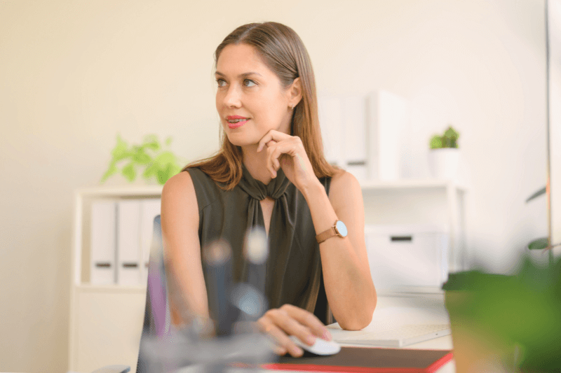 A professional woman sitting at her desk, thoughtfully reviewing property management tasks. The organized office setup includes plants and neatly arranged files, emphasizing a clean and efficient work environment. This image illustrates the dedication and attention to detail provided by Carolina Property Management Company when handling property management responsibilities, ensuring landlords receive expert service and support.